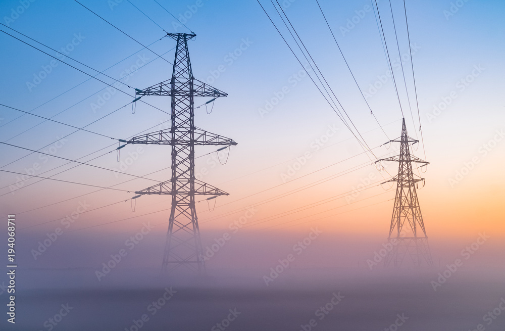 transmission towers in the fog at the background of the dawn sky. High Voltage power line silhouette during the sunset in a clear sky