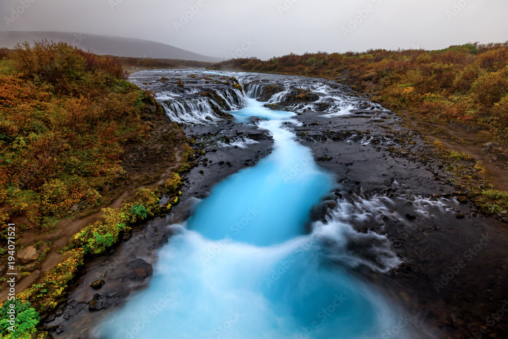 Bruarfoss, Iceland wide angle with it's dramatic and brilliant blue glacier water with fall colors lining the shores Bruarfoss, Iceland wide angle with it's dramatic and brilliant blue glacier water with fall colors lining the shores