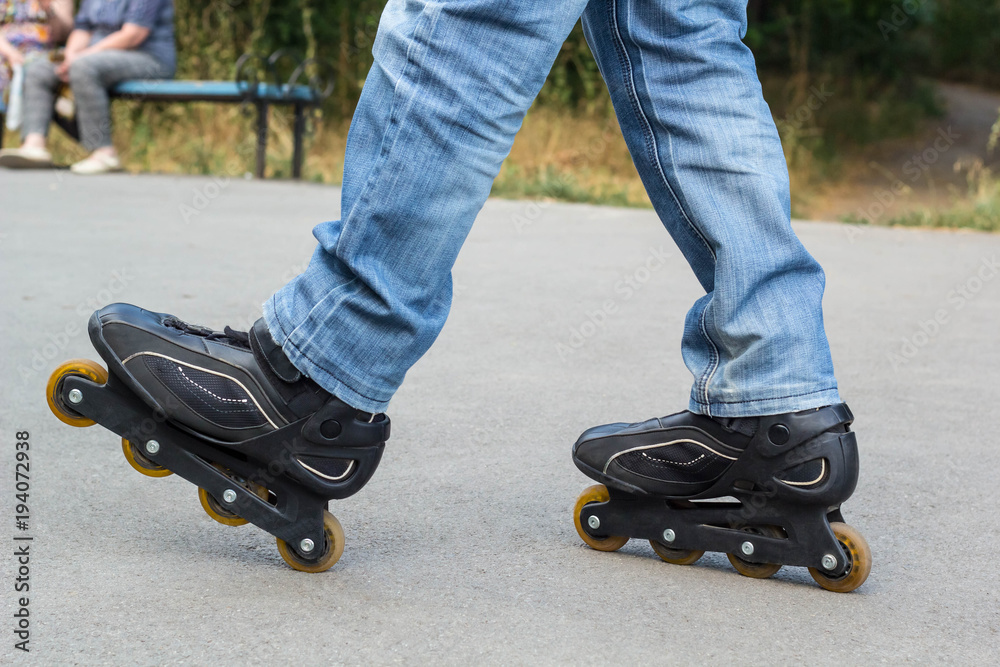 Young man in blue jeans riding roller skates in the city. Close up legs