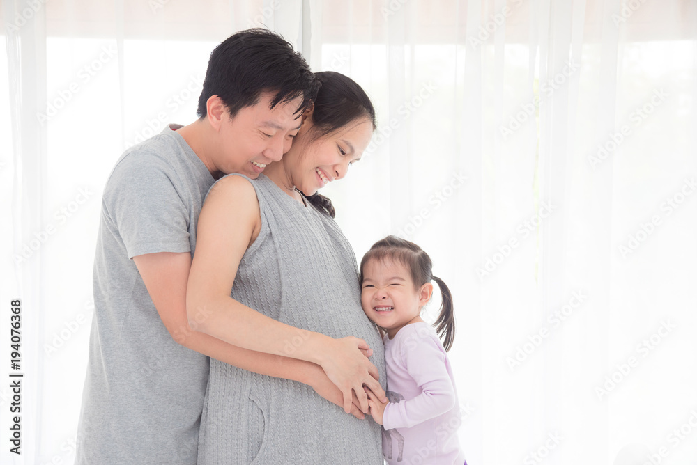 Asian man and his daughter hugging pregnant wife and smile together Asian man and his daughter hugging pregnant wife and smile together