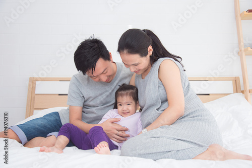 Asian father and mother sitting with their daughter on bed at home