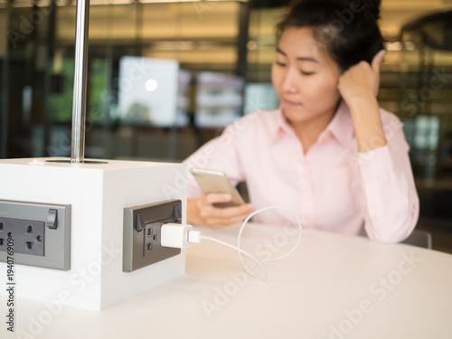 Asian female are looking at her smart phone. while a phone are charging with usb cable.