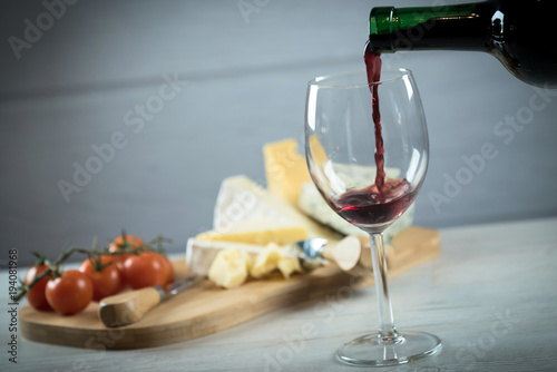 Red wine poured into a glass with cheese board 