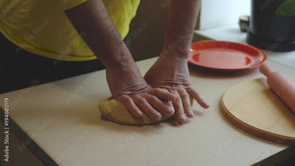 Male hands knead the dough on a white table, give it shape and put it on a red plate, top view. Cooking lenten bread at home for dietary nutrition. Male hands knead the dough on a white table, give it shape and put it on a red plate, top view. Cooking lenten bread at home for dietary nutrition.