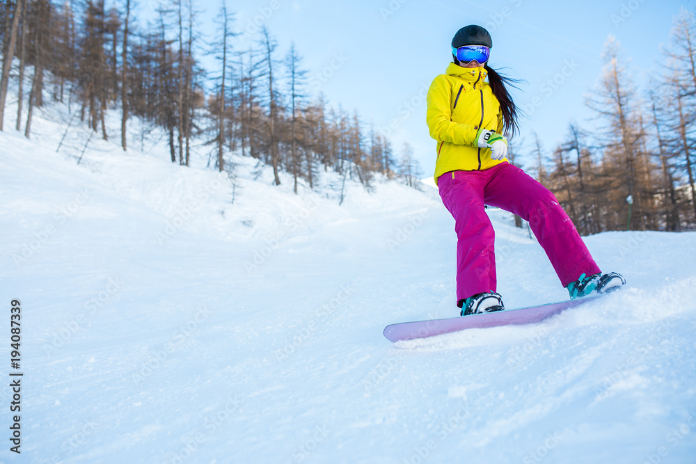 Image of athlete girl wearing helmet and mask snowboarding from snowy slope with trees