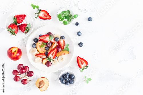 Fruit salad with strawberry, blueberry, peach, banana, grape and fresh fruits on white background. Flat lay, top view, copy space