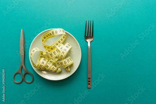 Tailor's meter on plate like chinese noodles with metal scissors and fork on green background. minimal concept. top view. diet, healthy food