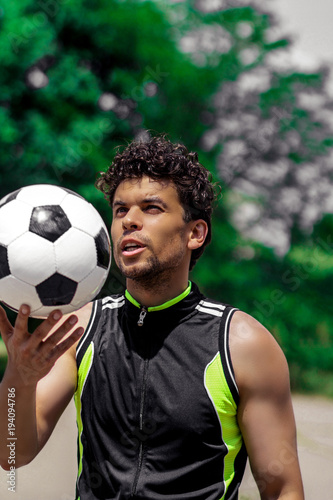 Tanned guy with curly hair in sports clothes, playing soccer ball © Dmitrii