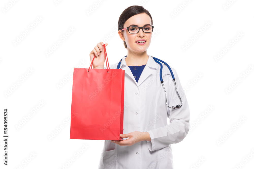 Successful young woman doctor with stethoscope offering shopping bag in white uniform on white background Successful young woman doctor with stethoscope offering shopping bag in white uniform on white background