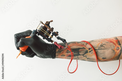 Man's hand holding tattoo machine on white background. the red wires