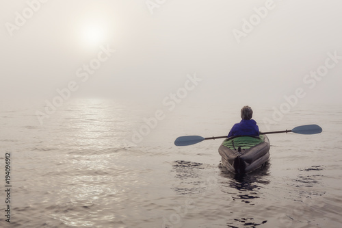 Girl kayaking on an inflatable kayak in Howe Sound during a fog covered winter sunset. Taken in West Vancouver, BC, Canada.