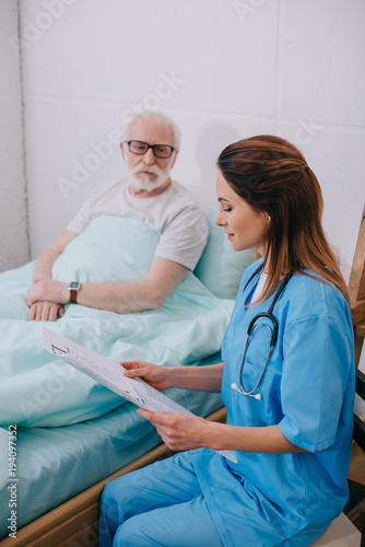 Nurse explaining medical advice to old patient in bed