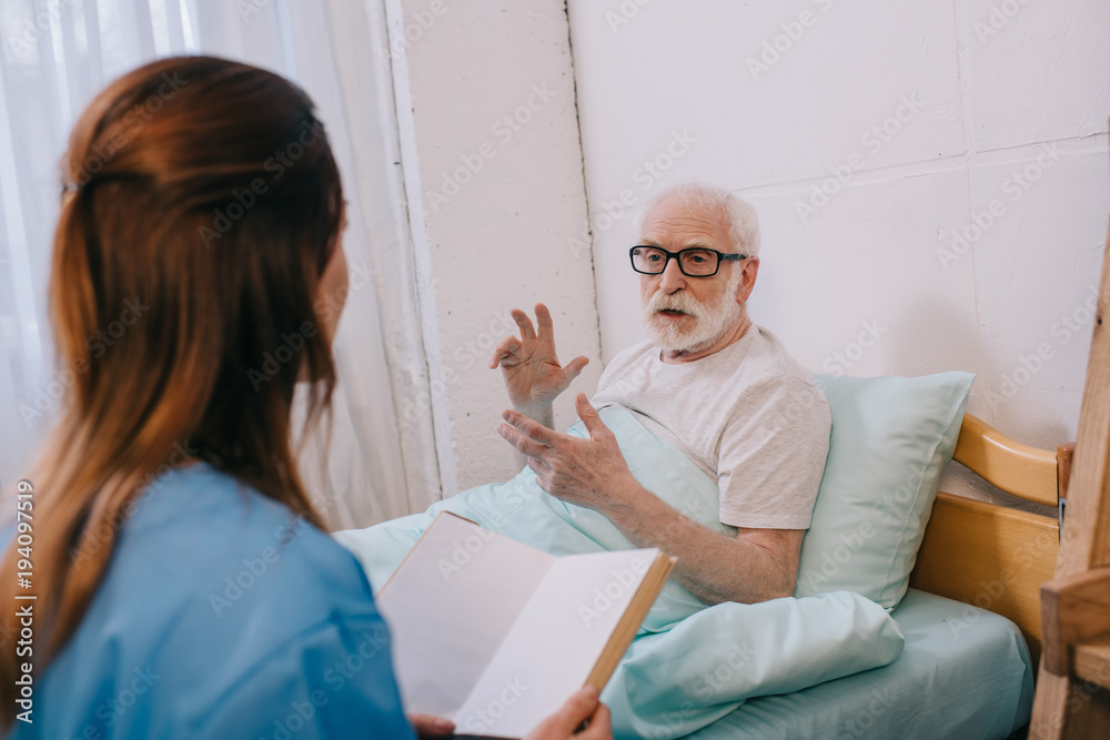Obraz premium Old man patient and nurse discussing plot of the book