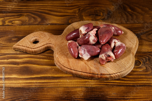 Raw chicken hearts on cutting board on wooden table