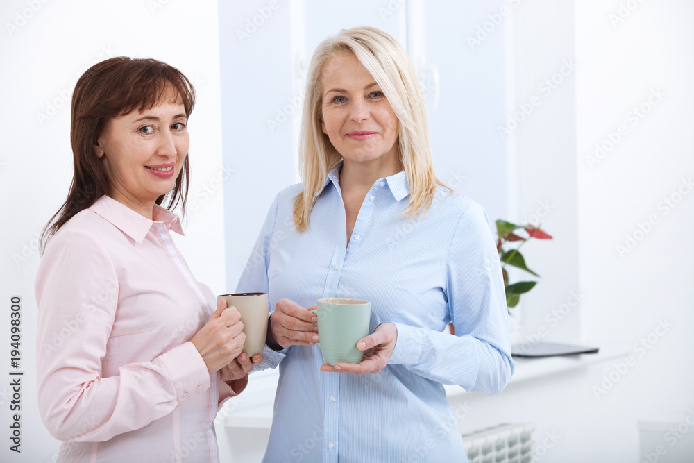 Office coffee break. Two female colleagues with cups of coffee talking. Office coffee break. Two female colleagues with cups of coffee talking.