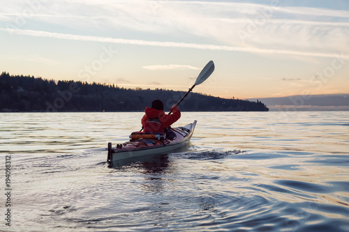 Man on Sea Kayak is kayaking during a vibrant winter sunset. Taken near Jericho Beach, Vancouver, BC, Canada.