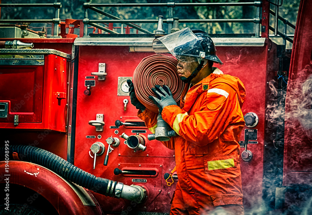 Fototapeta premium Emergency Fire Rescue training, firefighters in uniform, carry a water hose run through flame