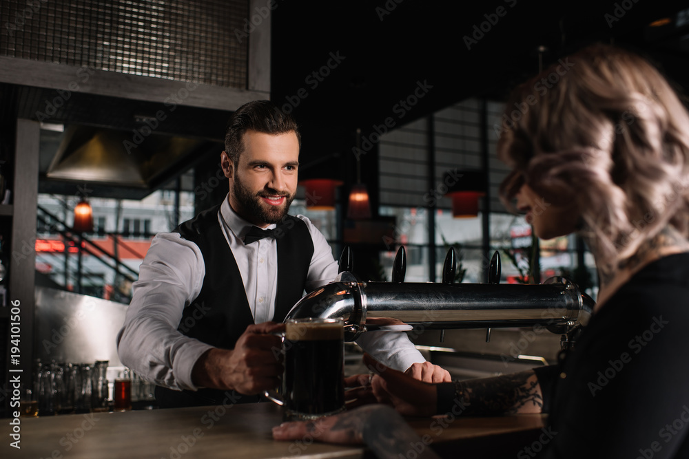 smiling handsome bartender giving glass of beer to female visitor