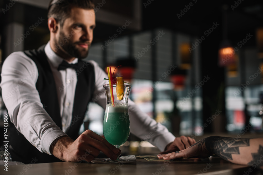 handsome bartender giving alcohol drink to girl at bar counter