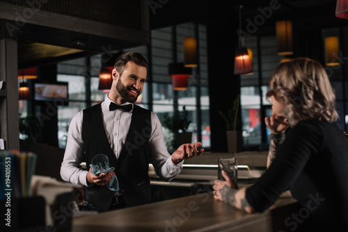 Quadro su tela smiling bartender cleaning glass and talking with female visitor