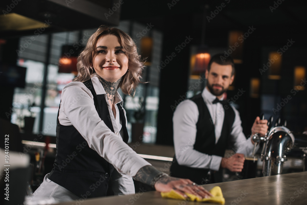 smiling bartender cleaning bar counter and looking away smiling bartender cleaning bar counter and looking away