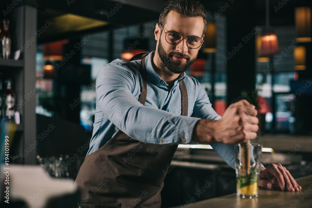 handsome bartender preparing alcohol drink and looking at camera handsome bartender preparing alcohol drink and looking at camera