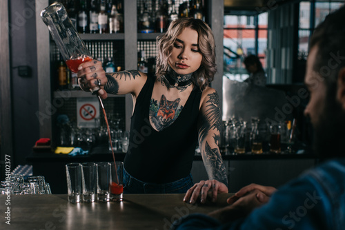 tattooed bartender making shot drinks for man at bar