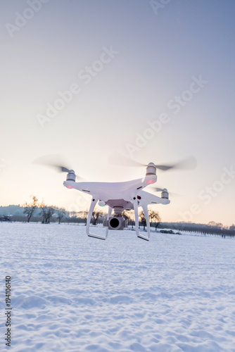 Fototapeta Naklejka Na Ścianę i Meble -  White drone camera floating in air with white snow and field in background