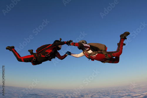 Two skydivers are in the winter sunset sky.