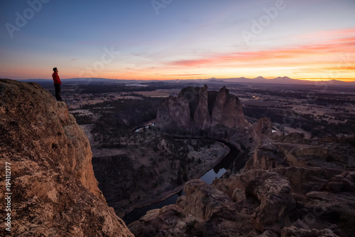 Man standing on top of a mountain is enjoying a beautiful landscape during a colorful and vibrant sunset. Taken at Smith Rock  Oregon  North America.