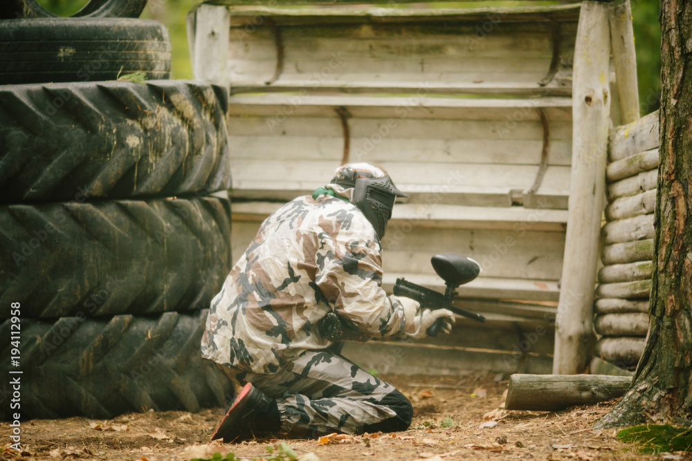 Fototapeta premium paintball player in protective uniform and mask aiming gun before shooting in summer.