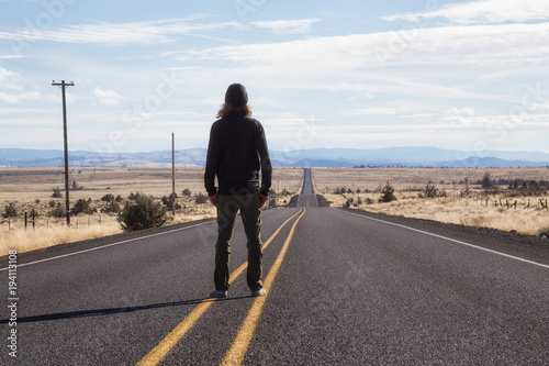 Man is standing in the middle of the long road during a vibrant sunny day. Taken in Oregon, North America. © edb3_16
