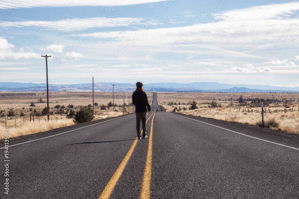 Man is standing in the middle of the long road during a vibrant sunny day. Taken in Oregon, North America.