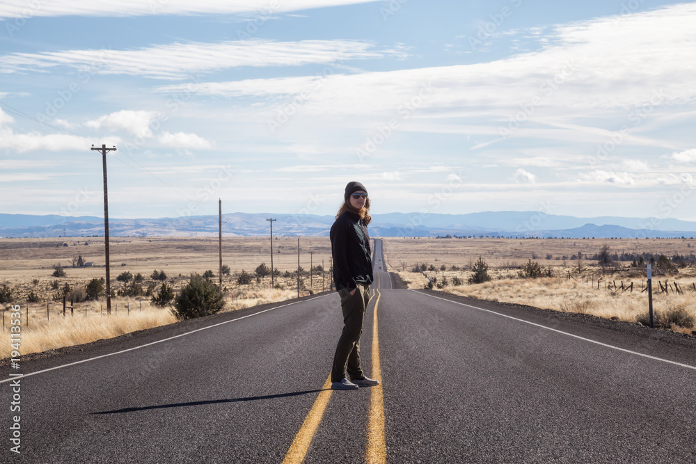 Man is standing in the middle of the long road during a vibrant sunny day. Taken in Oregon, North America.
