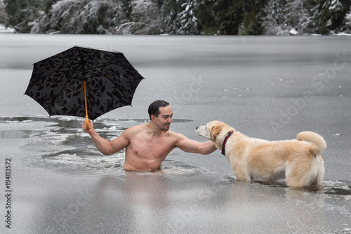 Bizarre picture of a man holiding an umbrella and petting a dog in a frozen lake. Taken in Alice Lake, Squamish, North of Vacouver, BC, Canada. photo