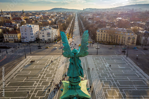 Budapest, Hungary - Angel sculpture from behind on the top of Heroes' Square at sunset with Andrassy street and the skyline of Budapest at background photo