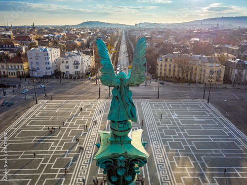 Budapest, Hungary - Angel sculpture from behind on the top of Heroes' Square at sunset with Andrassy street and the skyline of Budapest at background photo