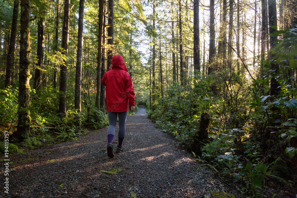 Obraz premium Girl wearing a bright red jacket is walking the the beautiful woods during a vibrant winter morning. Taken in Ucluelet, Vancouver Island, BC, Canada.