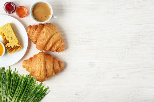 Croissants, coffee, honey, jam and sprouted wheat on a wooden background. Breakfast flat lay.