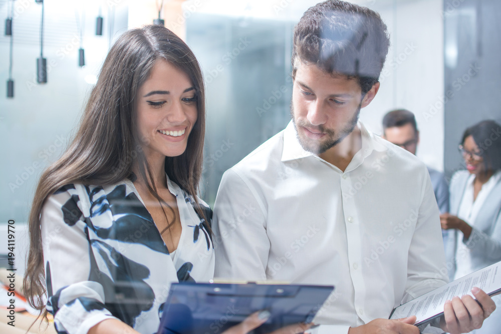 Fototapeta premium Portrait of smiling businesswoman showing financial report to her handsome male colleague at office.