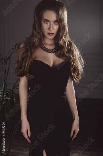 An attractive, slender, sexy brown-haired woman in a long black evening dress in the studio. Studio photo. Fashion photo.