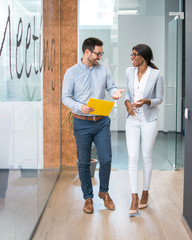 Two smiling business people walking through office hall and talking.