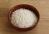 Stone bowl with uncooked white rice on wooden background