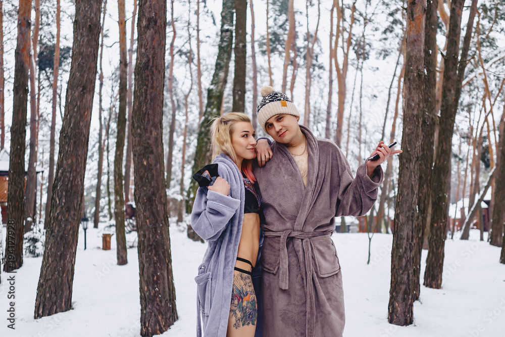 A beautiful couple in bathrobes in the middle of a pine forest on snow A beautiful couple in bathrobes in the middle of a pine forest on snow