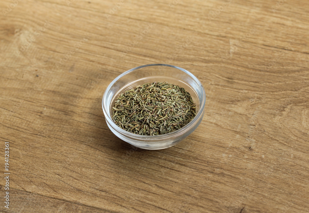 Glass of bowl of fresh sliced rosemary herbs on wooden background Glass of bowl of fresh sliced rosemary herbs on wooden background