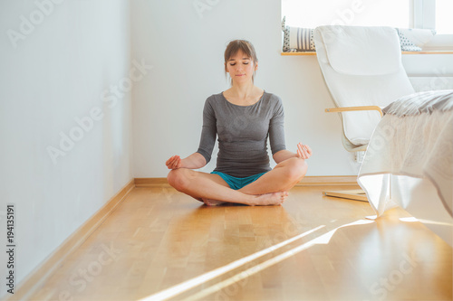 Woman wearing gray casual cloth practicing yoga exercise in morning after wake up, sitting on the floor at home or hotel bedroom.Healthy and sport lifestyle concept © Iryna