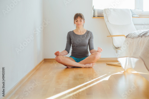 Woman wearing gray casual cloth practicing yoga exercise in morning after wake up, sitting on the floor at home or hotel bedroom.Healthy and sport lifestyle concept