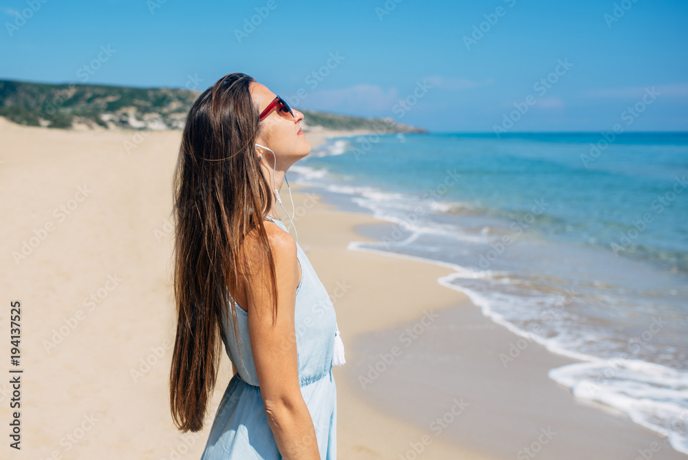 Girl in sunglass is standing on the beach and listening musi