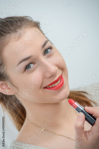 young and smiling woman putting lipstick