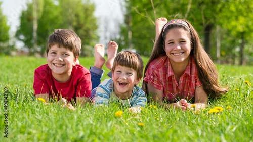 Three smiling kids lying together on green grass